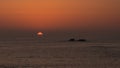 Sun disappearing below horizon at sunset on ocean with dark rocky islands in silhouette