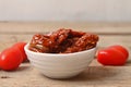 Sun dried tomatoes in white bowl on wooden table.