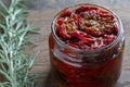 Sun-dried red tomatoes with garlic, green rosemary, olive oil and spices in a glass jar on a wooden table. Rustic style, closeup Royalty Free Stock Photo