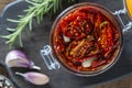Sun-dried red tomatoes with garlic, green rosemary, olive oil and spices in a glass jar on a wooden table. Rustic style, top view Royalty Free Stock Photo