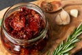 Sun-dried tomatoes with garlic, rosemary and spices in a glass jar on an olive wood cutting board Royalty Free Stock Photo