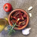 Sun-dried tomatoes with spices and garlic in a clay pot. Nearby is a bottle with olive oil, tomatoes, rosemary and garlic Royalty Free Stock Photo