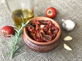 Sun-dried tomatoes with spices and garlic in a clay pot. Nearby is a bottle with olive oil, tomatoes, rosemary and garlic Royalty Free Stock Photo