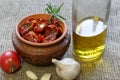 Sun-dried tomatoes with spices and garlic in a clay pot. Nearby is a bottle with olive oil, tomatoes, rosemary and garlic Royalty Free Stock Photo