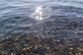 Sun glare and colorful pebbles in the silver clear blue water of lake baikal, ripples, shore