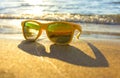 Sun glasses on beach near the sea. Yellow sunglasses on the background of sea wave on the shore of a tropical island Royalty Free Stock Photo