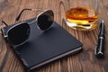 Sun glasses black notebook whiskey glass fountain pen natural wooden background Royalty Free Stock Photo