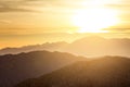 Sun glowing behind clouds and mountains in a desert landscape sc