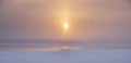 Sun in a haze at sunset over a frozen lake in snow and ice Royalty Free Stock Photo