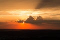 Sun hidden behind a large cloud mass in a blazing sky from yellow to red