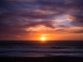 Sun on horizon at sunset with blue orange gradient sky and dark dramatic clouds over ocean