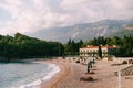 Sun loungers with folded sun umbrellas stand on the sandy beach near Villa Milocer. Montenegro