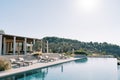 Sun loungers with folded sun umbrellas line the pillared terrace next to the long swimming pool. Hotel Amanzoe