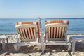 Sun loungers with orange mattresses on a sandy beach on the background of a calm blue sea. Idyll and relaxation. Space for text Royalty Free Stock Photo