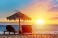 Sun loungers under umbrella on the sandy beach by the sea and sunset sky. Vacation background. Idyllic beach landscape on Mykonos Royalty Free Stock Photo