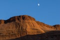 Sun lowers in sky and brightens a red rock escarpment under white moon Royalty Free Stock Photo