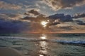 The sun over the sea shines through the clouds. Waves with foam roll on the sandy beach. Royalty Free Stock Photo