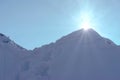 The sun peeking out from behind a snow-covered peak against a blue, slightly misty sky. Royalty Free Stock Photo