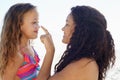 Sun protection is very important. A young girl poking her mothers nose while theyre at the beach.