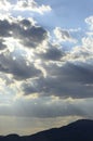 Sun rays beaming out from behind dark storm clouds over mountain range silhouette Royalty Free Stock Photo