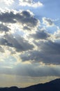 Sun rays beaming out from behind dark storm clouds over mountain range silhouette Royalty Free Stock Photo