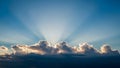Sun rays piercing through dramatic clouds at sunrise illuminating the vast blue sky above Royalty Free Stock Photo