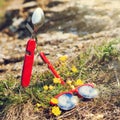 Sun-rimmed glasses with red rim lie on the green grass with yellow flowers, next to it is a penknife, fork and spoon, the concept