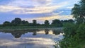 The sun rises among the clouds behind the trees above the river on a summer morning. Willows bow their branches over the water. Th Royalty Free Stock Photo