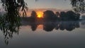 The sun rises among the trees growing on the far bank of the river. The morning mist spreads over the water. The branches of a ban Royalty Free Stock Photo