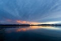 The sun rising over a lake with the colors of sunrise reflecting off the clouds and the water Royalty Free Stock Photo