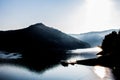 Sun rising over misty lake with mountain forest in the background and boat at the pier in the foreground Royalty Free Stock Photo