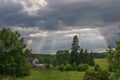 The sun`s rays break through thick dark clouds over the village, field and forest. Dawn, sunset. Horizontal photo Royalty Free Stock Photo