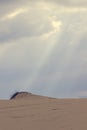 The sun`s rays through the clouds shine on the sand dune