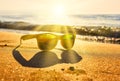 Sun`s rays cut through the stylish yellow sunglasses on the edge of the shore near the waves on sand. Royalty Free Stock Photo