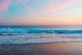 The sun sets over the tranquil beach, casting warm hues across the sky and reflecting its pink and golden glow on the waves Royalty Free Stock Photo