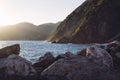 Sun setting against the Ligurian mountains by the ocean, creating golden vapors of waves hitting the rocks.