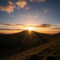 Sun setting behind a hill casting golden rays across the landscape Royalty Free Stock Photo