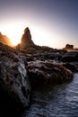 the sun setting behind a large rock out at the beach Royalty Free Stock Photo