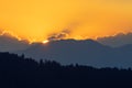 Sun setting behind mountain range and silhouette of spruce forest in foreground Royalty Free Stock Photo