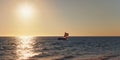 Sun setting down to calm sea, small sail piroga boat with silhouette of unknown man in distance Royalty Free Stock Photo