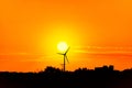 The sun is setting next to a windmill