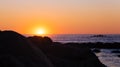 Sun setting on the ocean, behind a large rock in silhouette Royalty Free Stock Photo