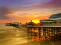 Sun setting over the historic north pier in blackpool with glowing golden light reflected on the beach and colourful twilight