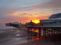 The sun setting over the historic north pier in blackpool with glowing light reflected on the beach and colourful twilight sky