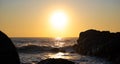 Sun setting over the ocean, with reflections on the ocean surface and dark rocks in silhouette Royalty Free Stock Photo