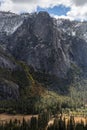 The sun shines on the colorful valley forest below while dark clouds cast a shadow on the tall snow dusted mountain peaks above