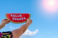 The sun shines. A piece of watermelon against a blue sky. Children`s hands are holding a slice of watermelon with the text Hello Royalty Free Stock Photo