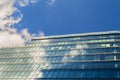 The sun is shining around the corner of a modern office building. The blue sky with clouds is reflected in the glass of identical Royalty Free Stock Photo