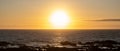 Sun shining brightly on horizon at sunset over ocean with golden reflections