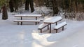 Sun shining on picnic benches and table covered with thick layer of snow in forest Royalty Free Stock Photo